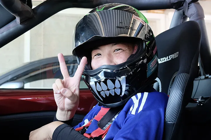 ヘルメット姿で運転席からピースサインをするドライバー