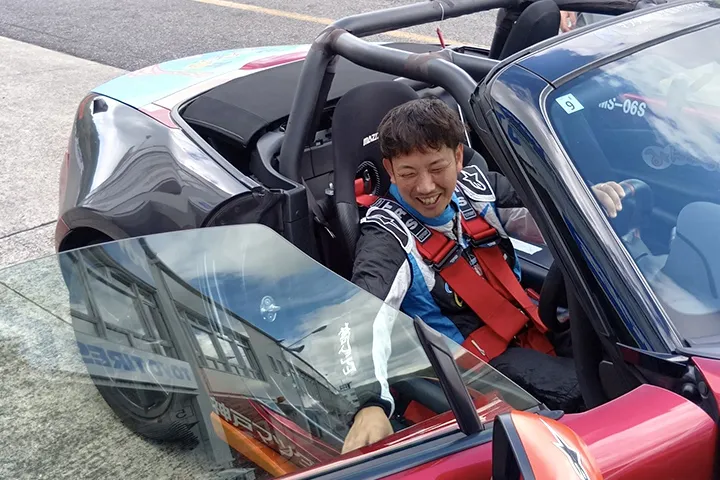シートベルトを締めたマシンの運転席で笑顔を見せるドライバー
